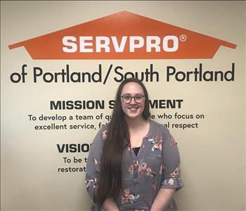 A lady with long brown hair standing near a SERVPRO wall