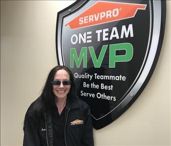 A lady with long hair standing in front of the SERVPRO one team sign