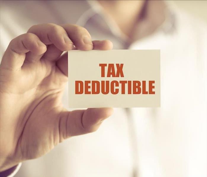 Closeup on businessman holding a card with text TAX DEDUCTIBLE, business concept image with soft focus background and vintage